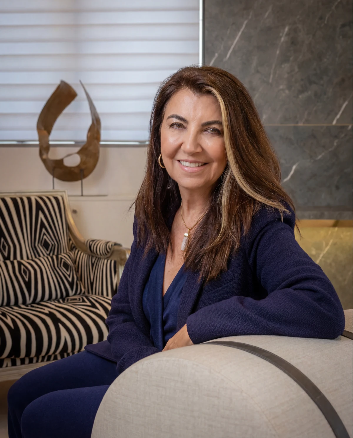 Retrato de Bianka Mugnatto, designer de interiores e fundadora da Interart, sentada em poltrona com escultura ao fundo
